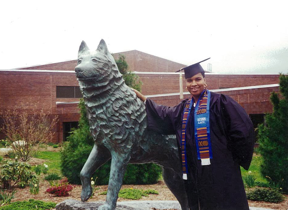 Jamelle Elliott in cap and gown beside the UConn Husky statue, graduation day